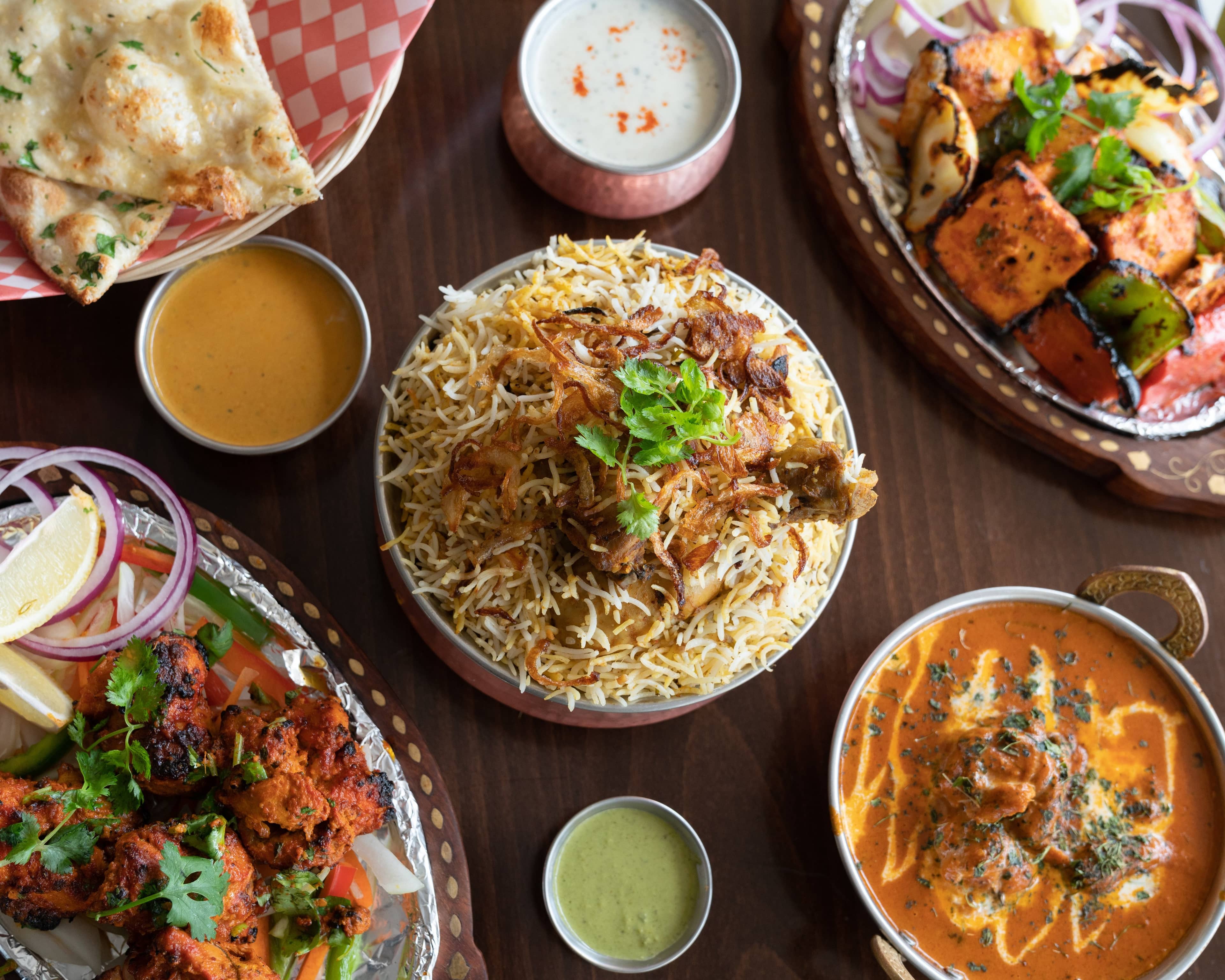 Overhead spread of biryani, naan, tandoori and curries on a table